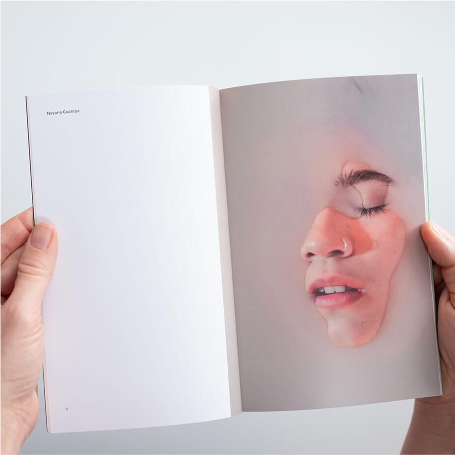Hands holding an open spread of WMN magazine, featuring a photo of face partially submerged in liquid